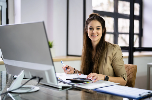 Female accountant working on capital accounting paperwork at desktop computer.