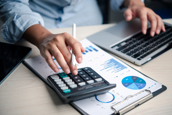 Person reviewing paperwork with laptop and calculator for cashflow forecast planning.