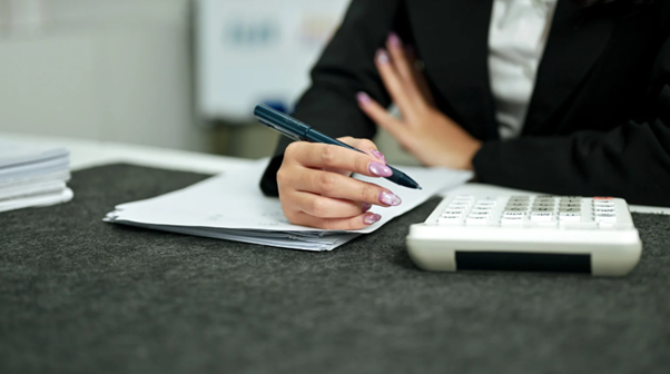 Person filling out tax return forms with papers, pen and calculator while checking tax return status.