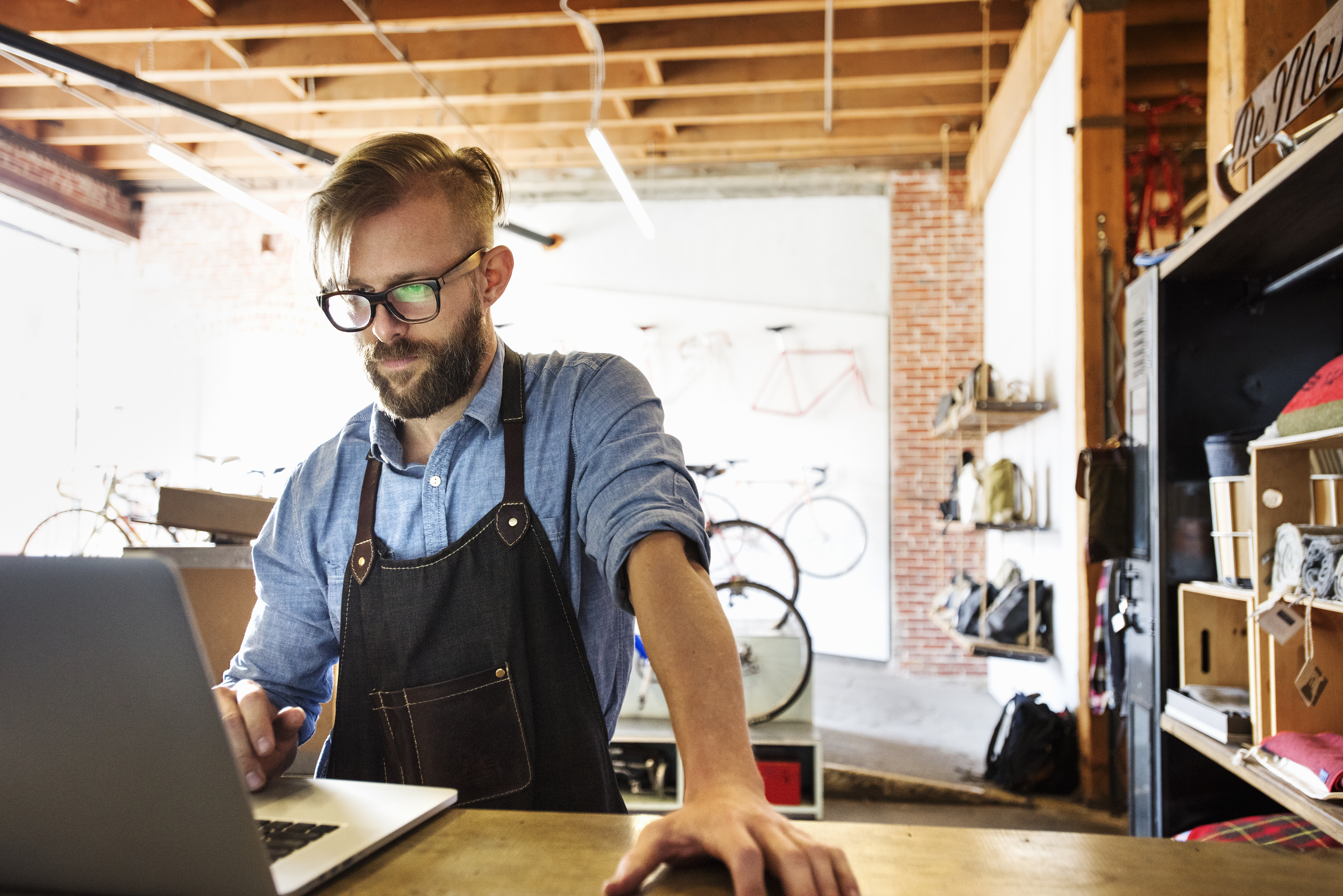 Small business owner using a laptop at a workshop counter, doing accounts for a limited company without professional help.