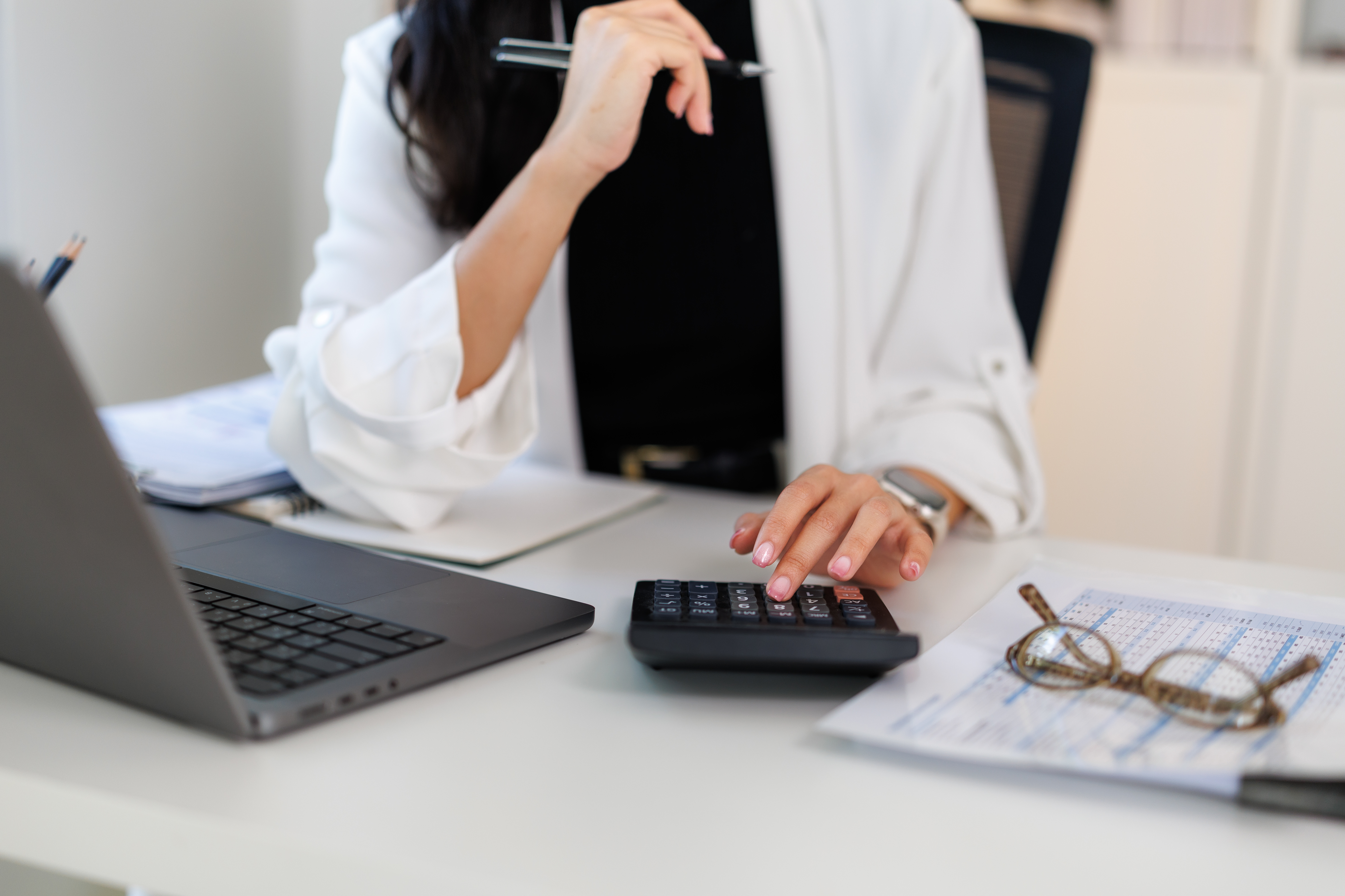 Businesswoman using a calculator alongside financial documents and a laptop, doing self assessment without an accountant.